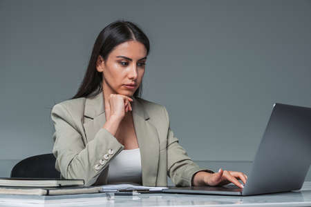 Businesswoman wearing formal wear is typing on laptop. Office workplace with desk and notebook in the background. Concept of working process of directorの写真素材