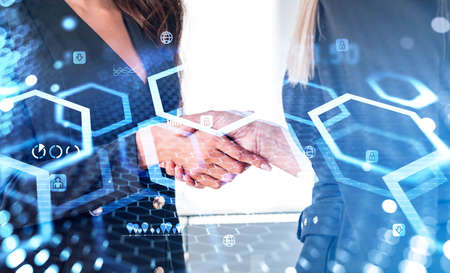 Businesswomen shaking hands, closeup, hud hologram and numbers with glowing blocks and different icons. Concept of cryptocurrency and agreementの写真素材
