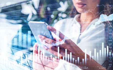 Office woman with phone in hands, stock market changes hologram. Double exposure of glowing bar chart with numbers and growing line. Concept of trading appの写真素材