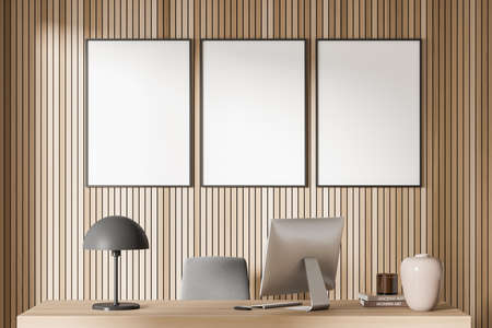 Light office room interior with table and pc with lamp. Decoration on wooden desk, books with candle. Mock up canvas frames on wooden wall in row, 3D renderingの写真素材