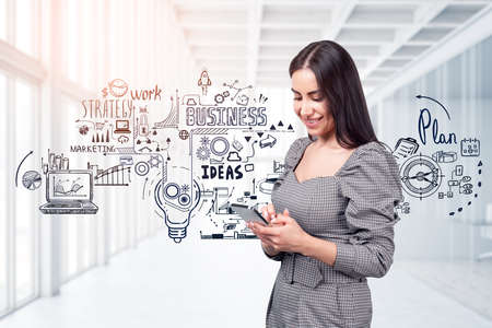 Smiling young attractive businesswoman wearing formal dress is typing message on smartphone. Sketch with light bulb, pie and bar diagrams, rocket start up in the background. Concept of communicationの写真素材