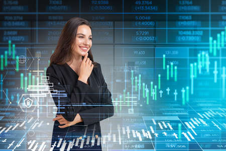 Smiling young attractive businesswoman wearing formal suit is touching her chin. Panoramic window in background. Financial chart and forex candlestick in foreground. Concept of international tradingの写真素材