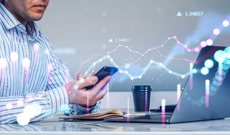 Office man hand using mobile app, laptop and notebook on the table, double exposure with glowing rising lines and numbers. Concept of financial analysis and online tradingの写真素材