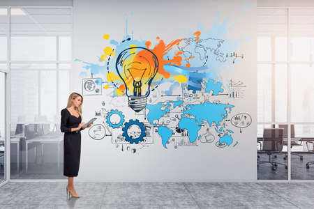 Young attractive businesswoman wearing formal dress is typing message on tablet. Sketch with light bulb, international map and globe, bar and pie diagrams. Concept of imagination for creative ideasの写真素材