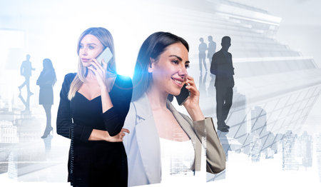 Two businesswomen wearing formal wear are talking on smartphones. Singapore city skyscraper financial downtown in the background. Concept of working process in international company and teamworkの写真素材