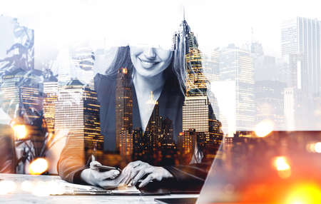 Businesswoman wearing formal suit is typing message on smartphone. Office workplace and New York city skyscraper panoramic view in the background. Concept of working processの写真素材