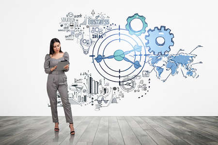 Office woman with digital device in hands, full length on parquet floor, business strategy on white wall. Start up doodle plan with financial chart and gears, analysis. Concept of planning and goalの写真素材