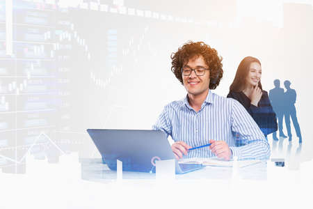 Smiling man with laptop and woman, silhouette of business people, blurred hologram of financial...
