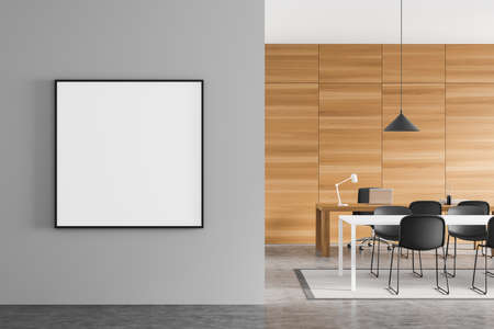 Empty square canvas on gray wall next to manager office with meeting table and personal desk. Modern...
