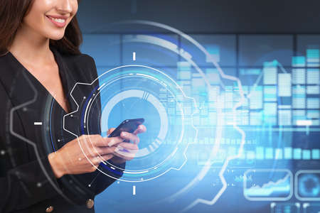 Smiling businesswoman wearing formal suit is holding smartphone. Digital interface with circle hologram and hud in the background. Concept of modern technologies in businessの写真素材