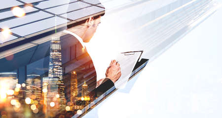 City skyscraper downtown panoramic view. Young serious businessman taking notes on clipboard. Concept of working process and trading in modern megapolisの写真素材