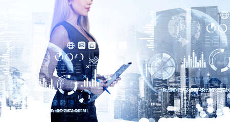 Smiling businesswoman wearing formal wear is holding clipboard. New York city skyscrapers in the background. Digital interface with bar and pie diagrams, virtual globe and icons of message and emailの写真素材