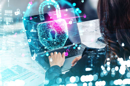 Businesswoman wearing formal suit is working on laptop with cyber protected files. Digital interface with hologram of padlock and virtual globe in the foreground. New York city in the backgroundの写真素材