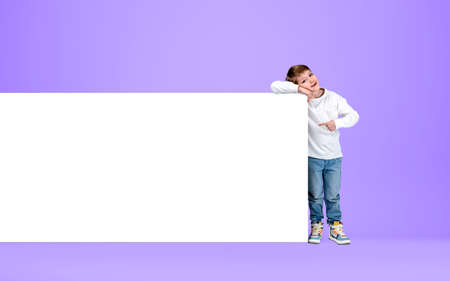 Boy kid smiling, finger point at empty whiteboard, mockup canvas on purple background. Concept of...