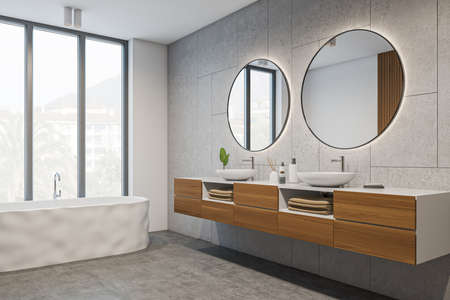 Corner view on bright bathroom interior with bathtub, panoramic window with town view, two round mirrors and sinks, white walls and concrete floor. Hygienic and procedures for health. 3d renderingの写真素材