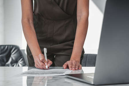 Office woman hand with pen writing in a paper, closeup, business report on desk. Concept of...