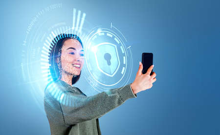 Attractive businesswoman wearing casual wear is holding smartphone scanning face with digital...