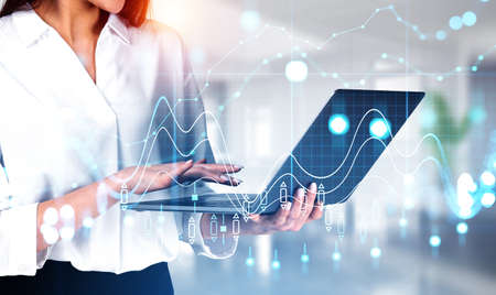 Businesswoman hands typing on laptop, blurred office room. Stock market changes, forex candlesticks virtual screen hologram with chart and lines. Concept of online tradingの写真素材