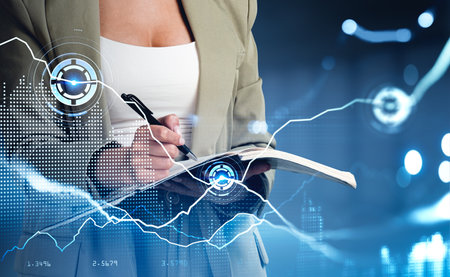 Businesswoman wearing formal wear is taking notes in notebook. dark blue background. Digital interface with hologram of pie diagrams, network connection. Concept of cyberspace and modern technologyの写真素材