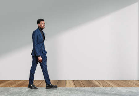 African businessman in blue suit, pensive look, walking on tile floor. Concept of career development...