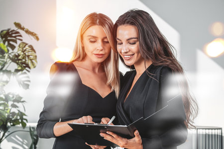 Two office women with clipboard in business room, take note, studying documents, reading financial report. Concept of teamwork and analysisの写真素材