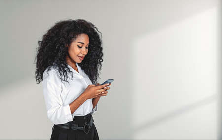 Smiling african businesswoman working with phone, light background. Concept of communication and...