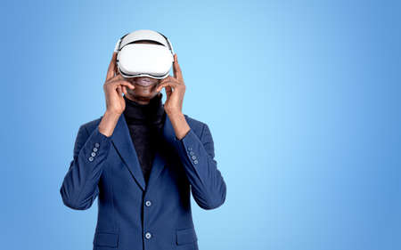 African businessman working in vr glasses headset, standing on light blue background. Concept of metaverse and information fields. copy spaceの写真素材