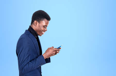 Young black businessman profile with a happy smile browse smartphone, light blue background. Concept...