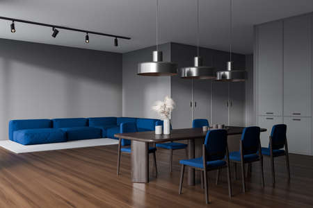 Dark kitchen interior with sofa in the corner, dining table with blue chairs, side view, hardwood...