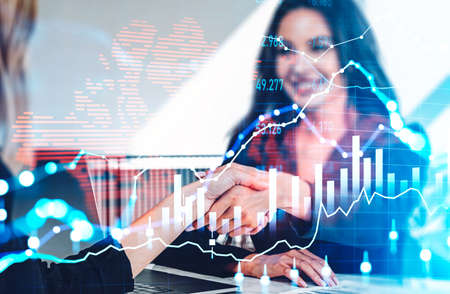 Businesswomen shake hands in office room. Double exposure of forex diagrams, stock market...
