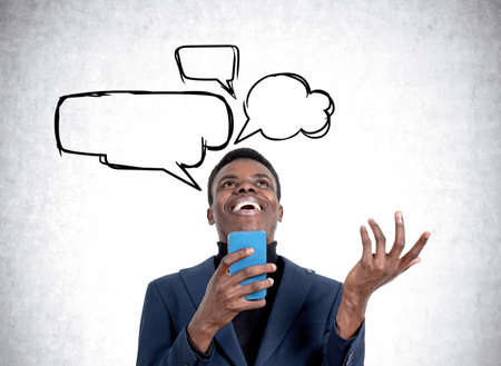 Happy laughing black businessman having a video call and hand gesturing on gray concrete background. Concept of eureka and idea. Copy space bubble thoughtの写真素材