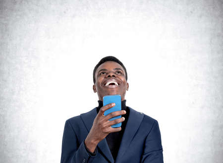 African American handsome businessman wearing formal wear is laughing holding smartphone near...
