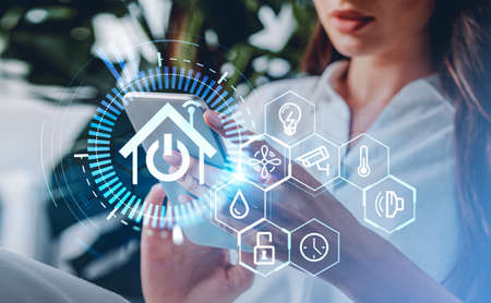 Woman using smartphone, glowing house hud with diverse icons, interface and binary. Concept of remote control and smart homeの写真素材