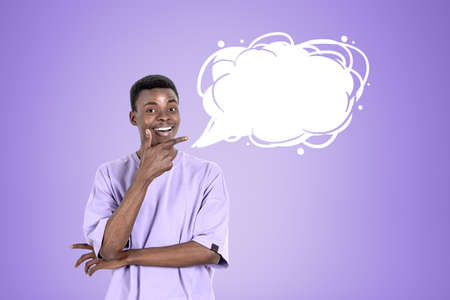 Black young man in purple t-shirt, smiling with inspired look, finger pointing to the mockup blank...