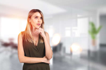 Pondering attractive businesswoman wearing formal wear is standing touching chin at office workplace in background. Concept of model, successful business personの写真素材