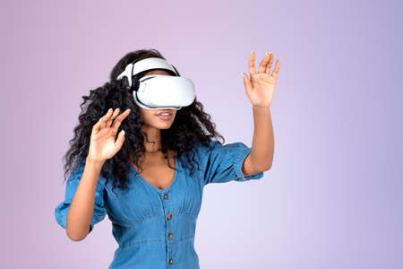 African young woman wearing vr glasses headset, fingers touching something on pink background....