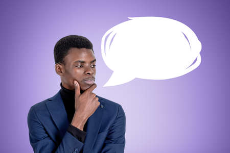 Pondering African American businessman wearing formal wear is standing touching chin near empty...