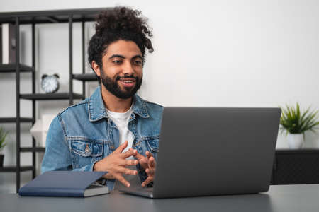 Smiling handsome businessman in casual wear is sitting having online conference call at office...