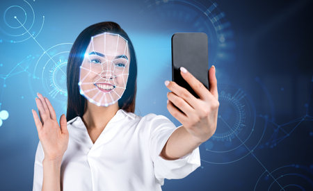 Smiling attractive businesswoman wearing formal wear is taking selfie via smartphone. Circle hologram with line connection. Concept of facial recognition, biometric scanning, mobile unlockの写真素材
