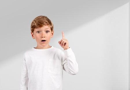 Child boy with eyes wide open and finger pointing up, amazed look light copy space background. Concept of idea and planの写真素材