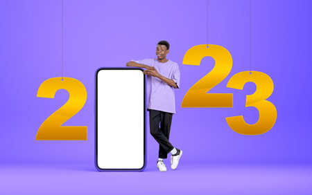 Young black man hand pointing at smartphone, full length standing with 2023 year numbers hanging....