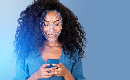 Smiling African American businesswoman typing on smartphone with facial recognition by digital interface with line connection hologram. Concept of modern technology of artificial intelligenceの写真素材
