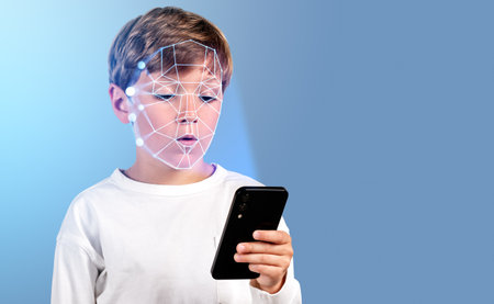 Concentrated boy with smartphone in hand, digital biometric scanning hologram. Face detection and recognition. Concept of face id and educationの写真素材
