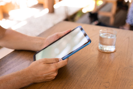Man hands holding tablet with mock up blank screen, glass of water on wooden desk. Concept of online...