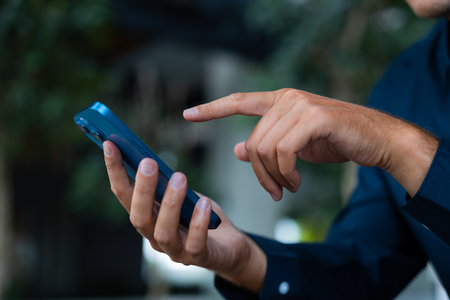 Man finger point and touch phone closeup, blue shirt and blurred background of green leaves. Concept of online communication, shopping and applicationの写真素材