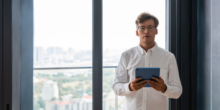 Businessman in eyeglasses and white shirt holding tablet in hands. Portrait looking at the camera,...