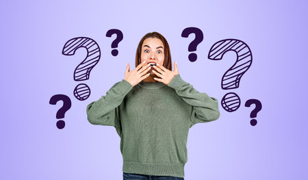 Portrait of astonished young woman in green sweater with hands near open mouth over purple...