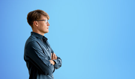 Portrait of confident young European businessman standing with crossed arms over blue background....