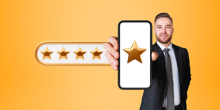 Smiling young bearded European businessman showing smartphone with five star rating standing over...