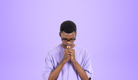 Portrait of young African man college student in casual clothes and glasses thinking hard standing over purple background. Concept of brainstorming and career choiceの写真素材